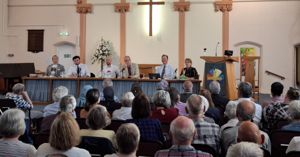 A crowd of people attend a hustings event before a line of parliamentary candidates in a church building