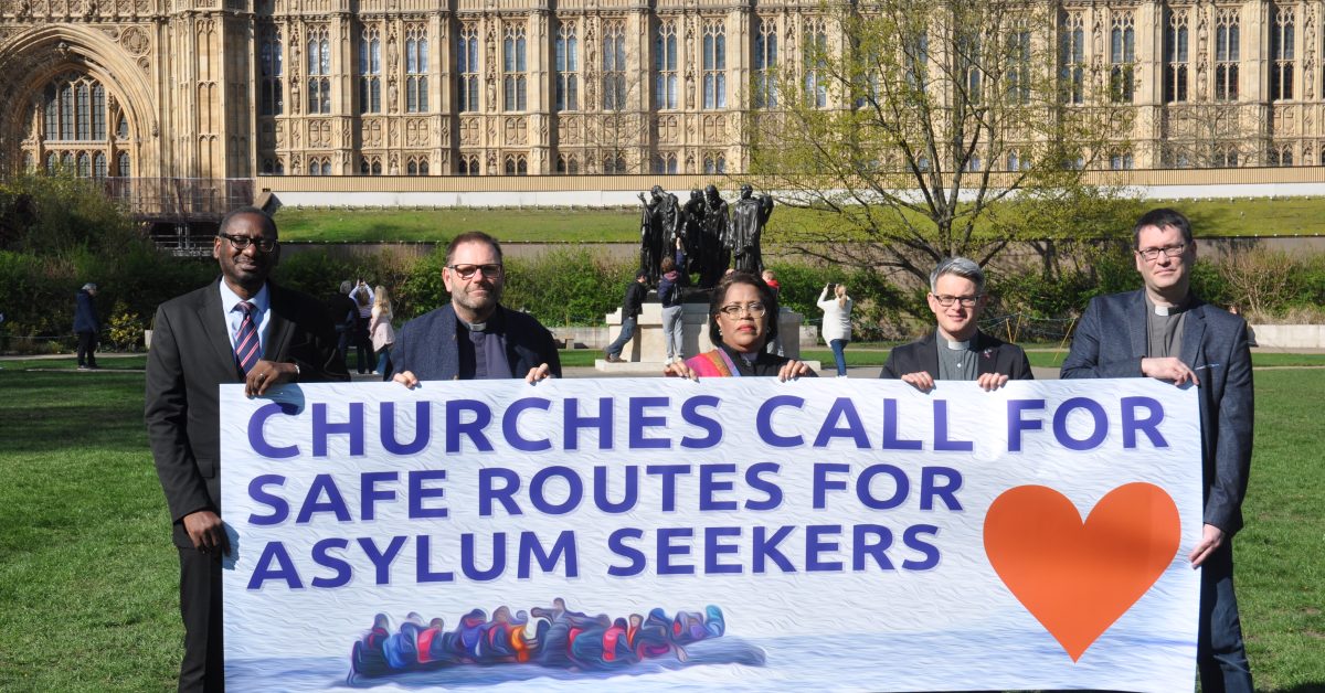 Five church leaders stand in front of parliament holding a banner saying 'Churches call for safe routes for asylum seekers'