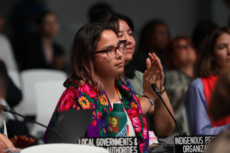 Photograph from COP28, of 2 people behind the Indigenous Peoples organisations sign