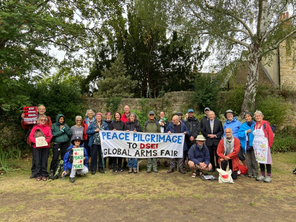The group of peace pilgrims to the arms fair holding a banner standing in front of some trees