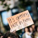 A cardboard protest sign that reads "It's getting hot in here"
